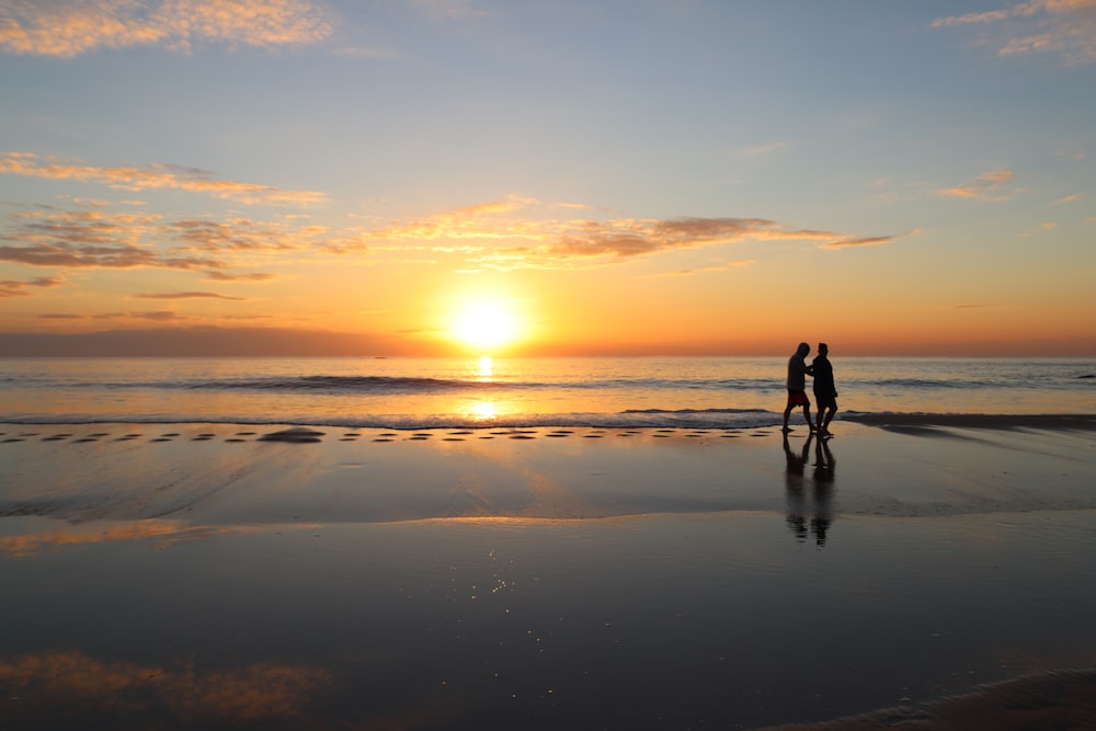 silhouette of 2 person walking on beach during sunset