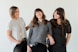 3 women smiling and standing beside white wall