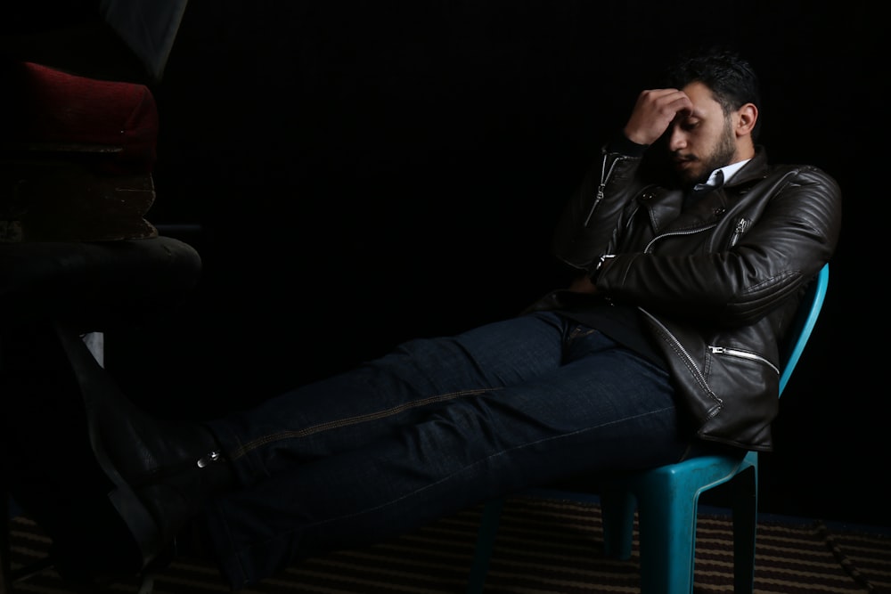 man in black leather jacket sitting on blue plastic chair
