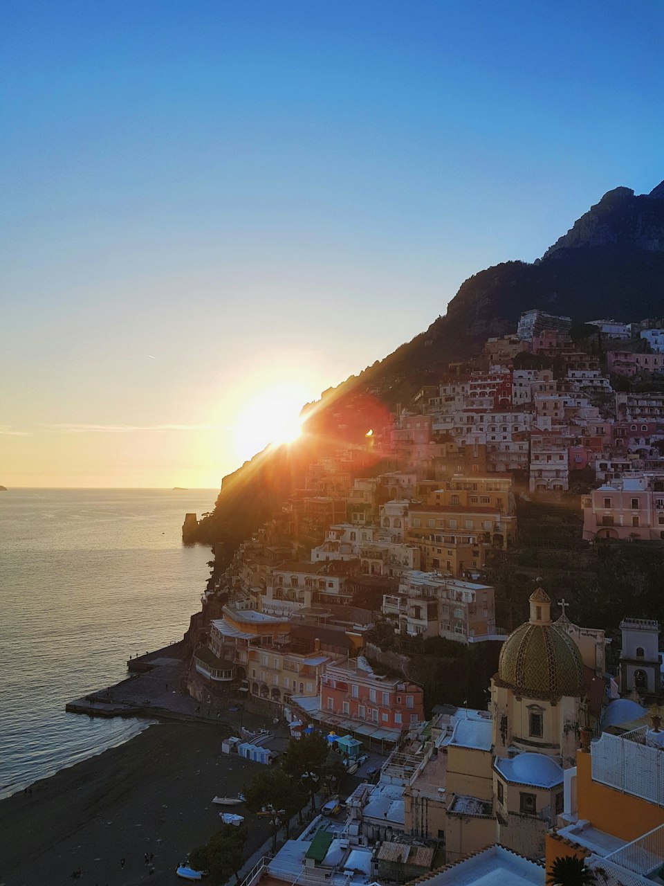 The sun rising behind Positano's cliffside houses and domed church