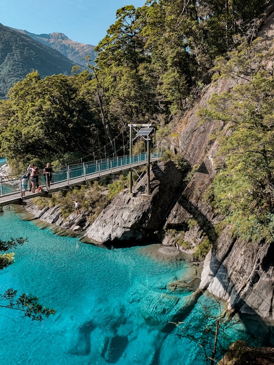 people walking on bridge over river during daytime in Mount Aspiring New Zealand