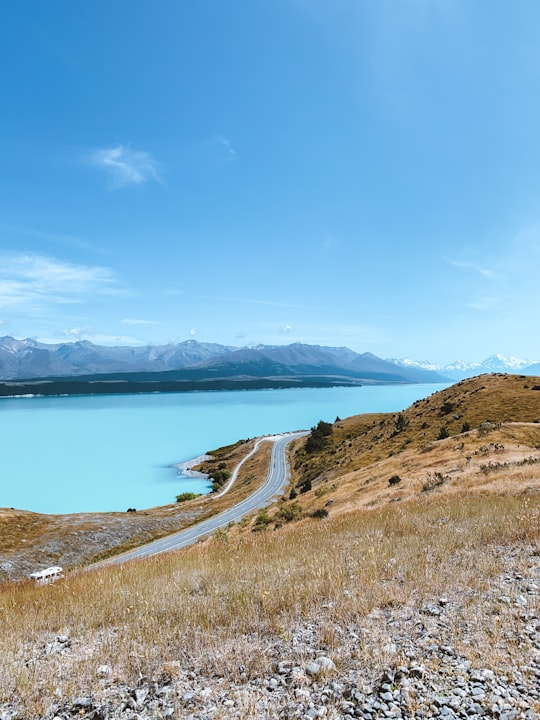 brown grass field near body of water under blue sky during daytime in Lake Pukaki New Zealand
