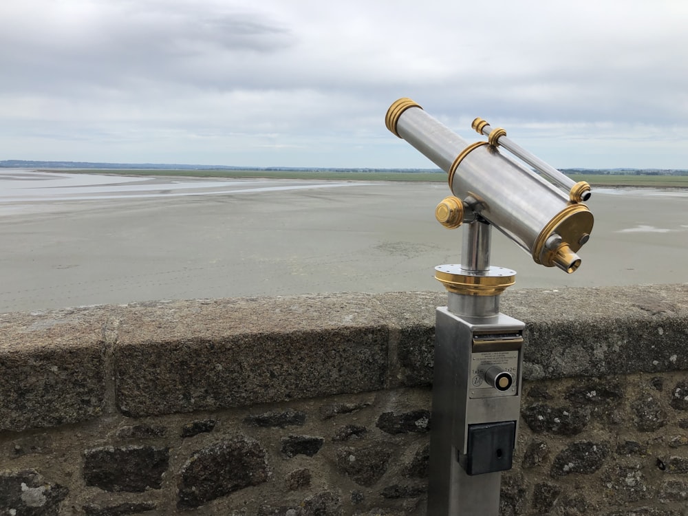 telescópio de aço inoxidável na parede de concreto cinzenta perto do mar durante o dia