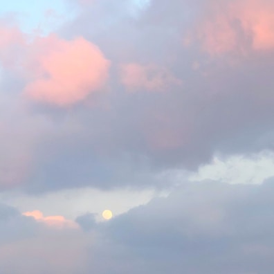 Soft, pastel-colored clouds fill the sky, with a prominent pink hue blending into a gentle blue. A faint moon peeks through the clouds, adding a subtle focal point.