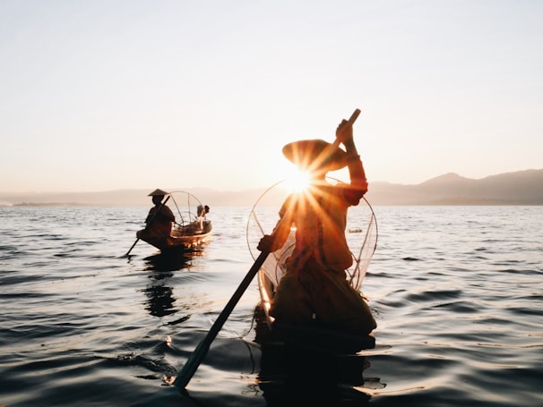 silhouette of 2 men riding on boat during sunset