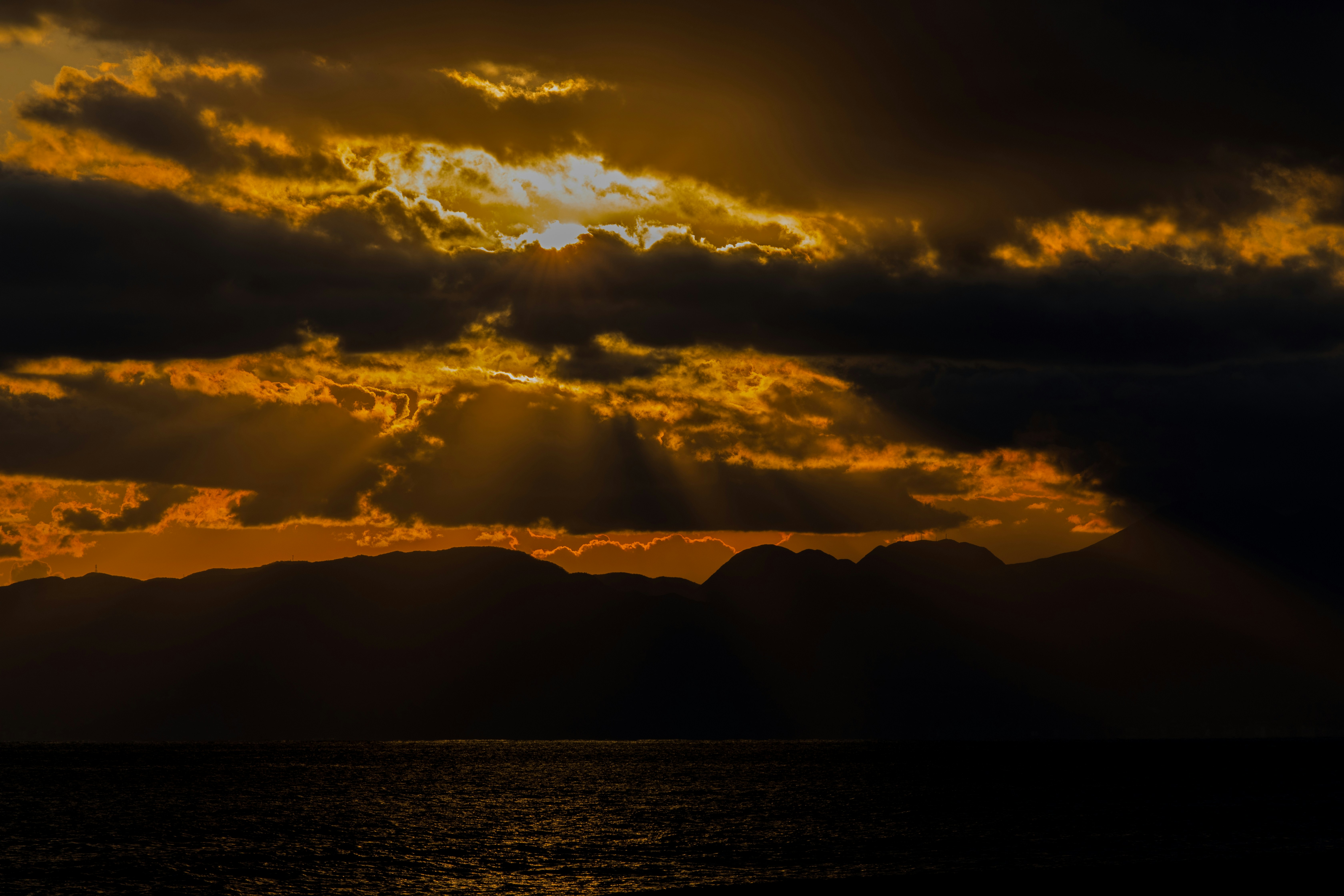 silhouette of mountains near body of water during sunset