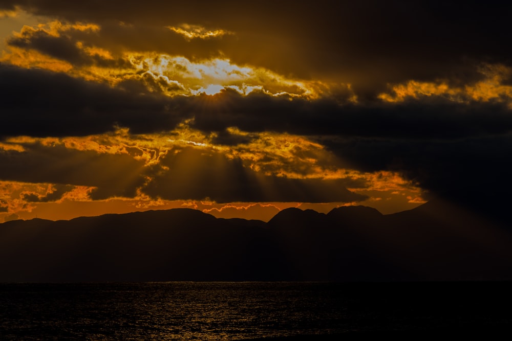 silhouette of mountains near body of water during sunset