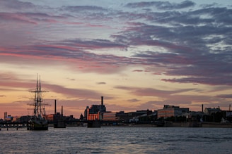 A panoramic view of a ship anchored at a bustling port during sunset.