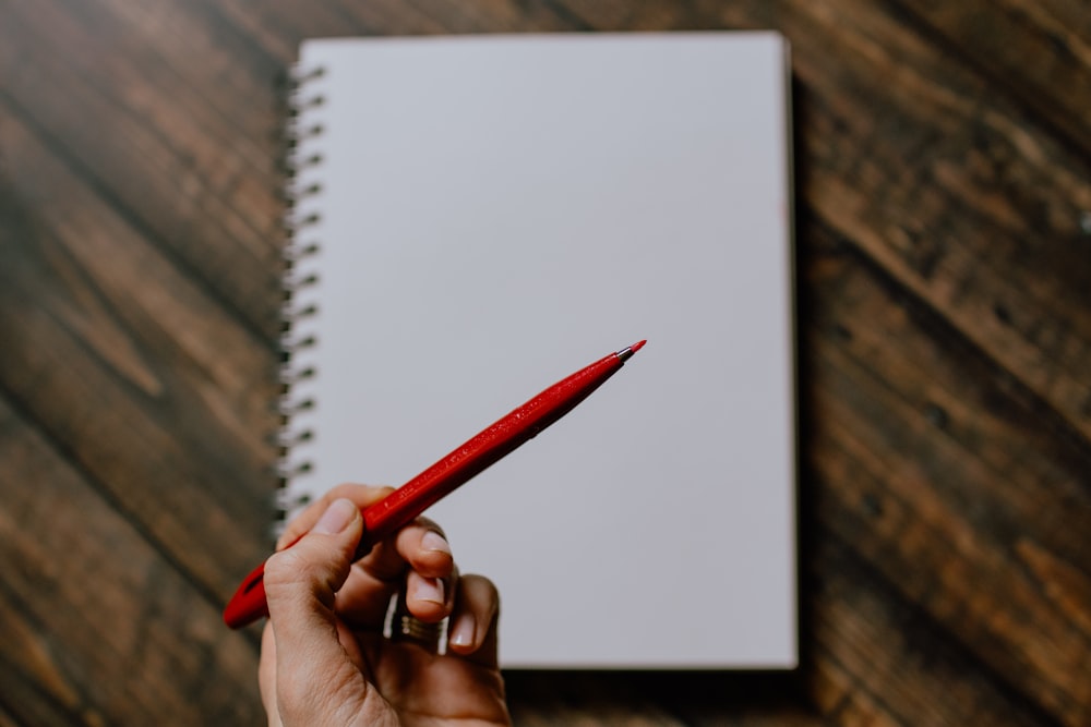 person holding red pencil writing on white paper