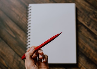 person holding red pencil writing on white paper