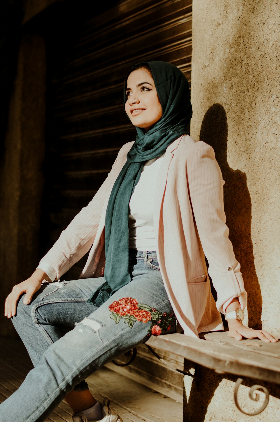 woman in white long sleeve shirt and blue denim jeans sitting on brown concrete wall