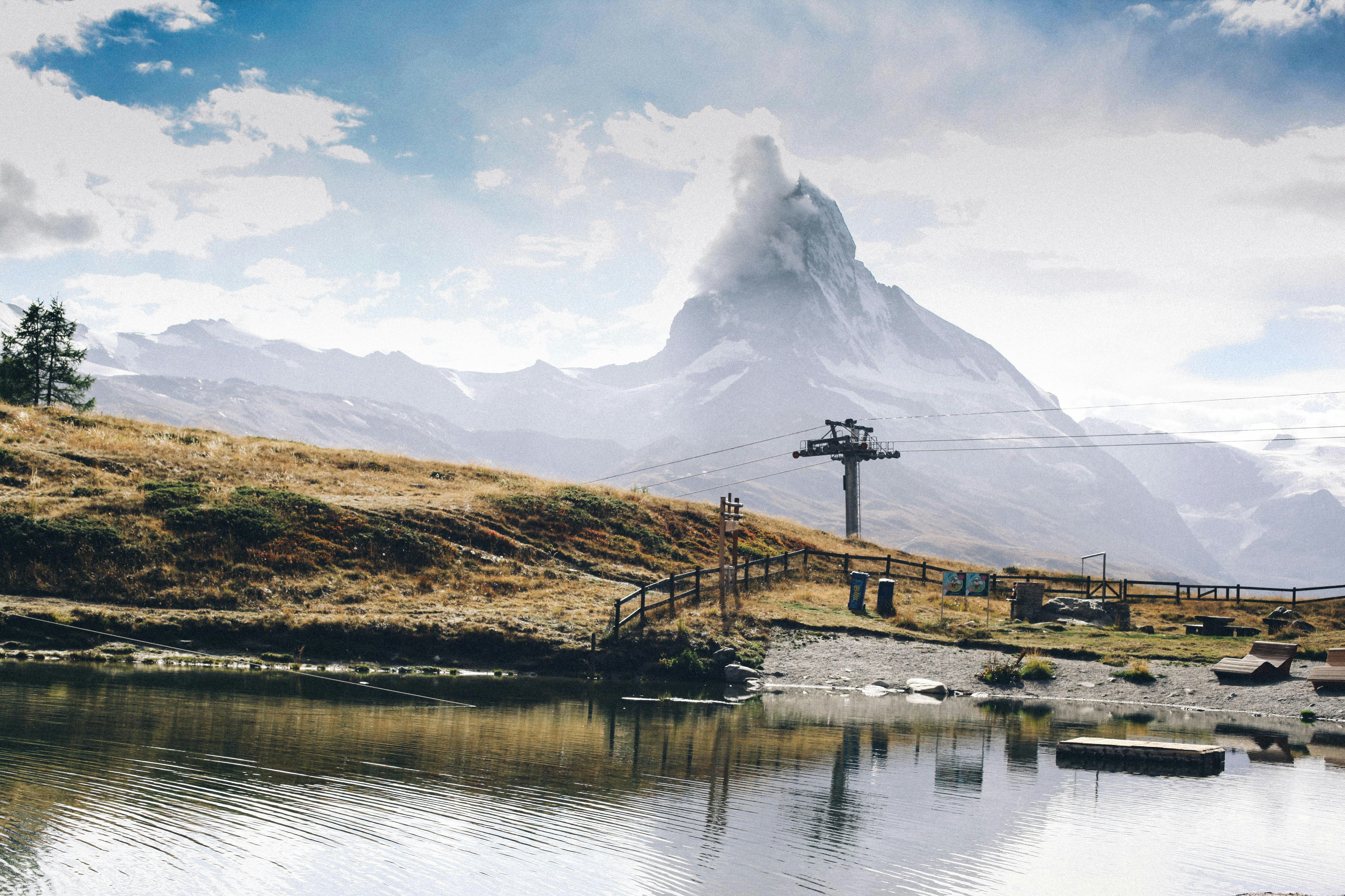 brown grass field near lake and mountain under white clouds and blue sky during daytime