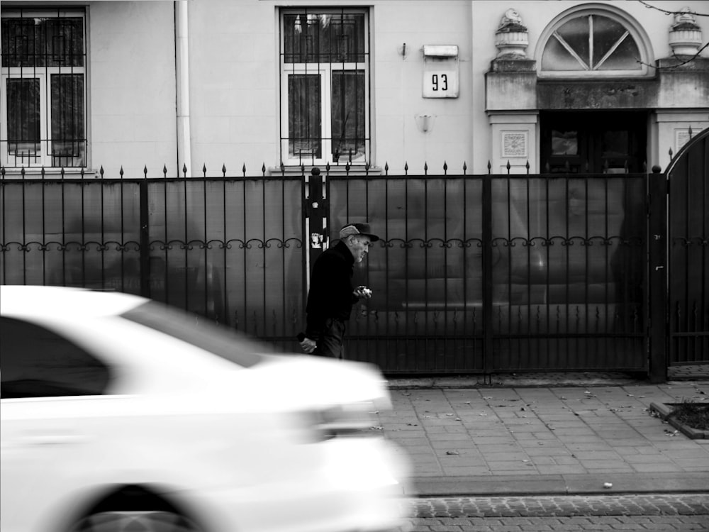 grayscale photo of man walking on sidewalk