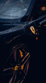 Photographer capturing a luxury car's reflection on a wet asphalt surface.