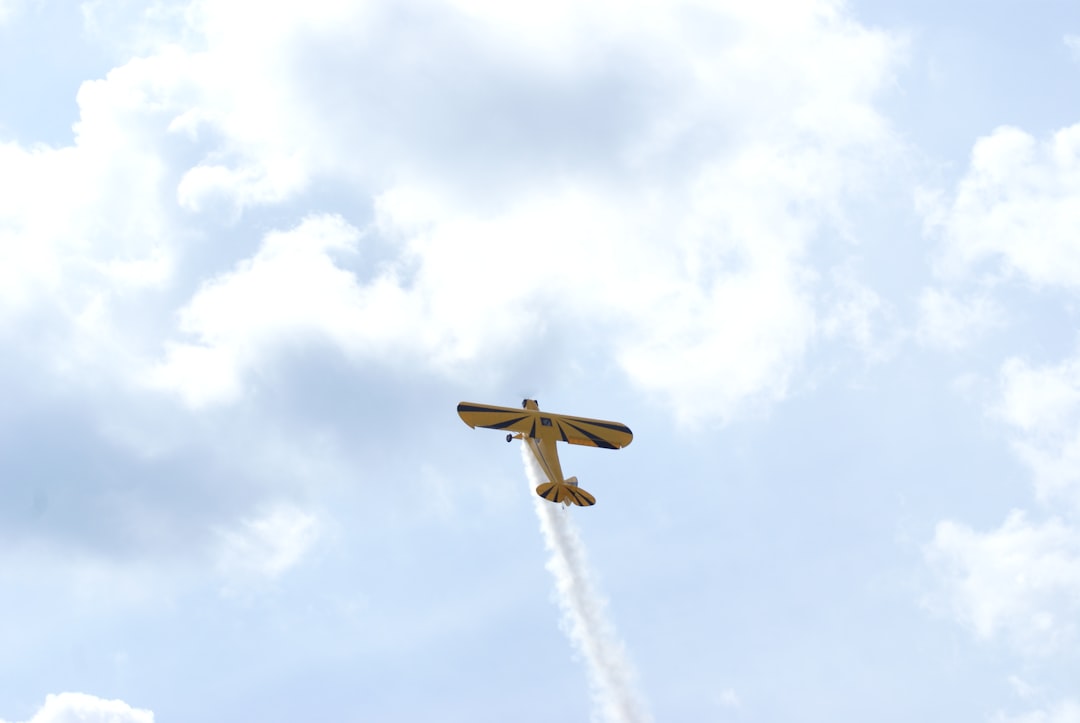 brown and white plane flying under white clouds during daytime