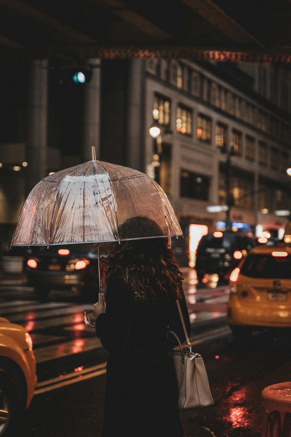 Person im schwarzen Mantel, die nachts Regenschirm hält