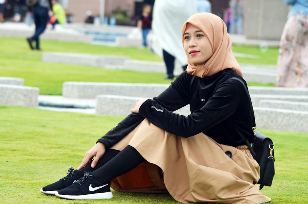 Femme en abaya noire et blanche assise sur un champ d’herbe verte pendant la journée