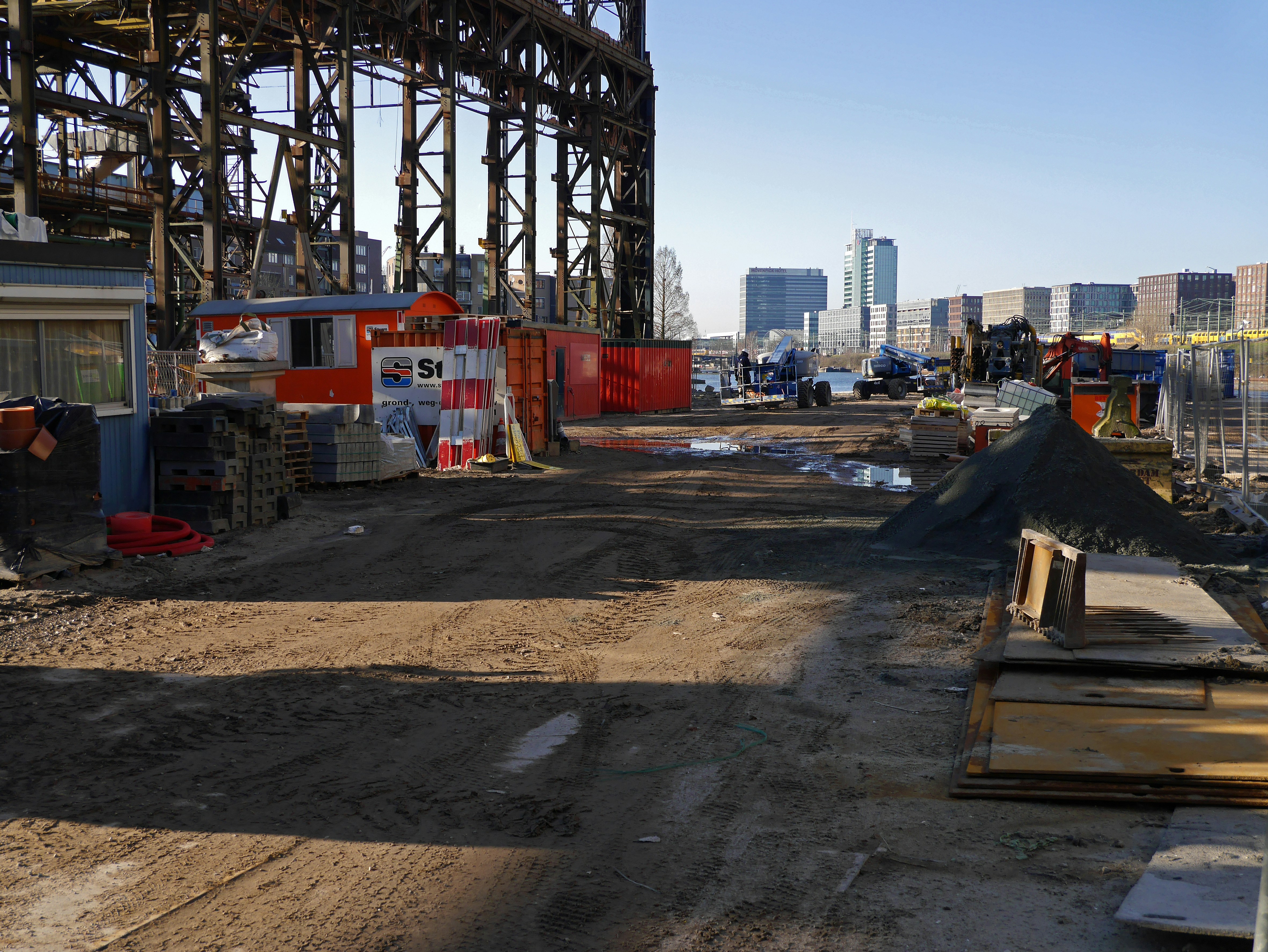 Construction materials stacked on site in bright daylight, organized cement bags and steel rods, clear sky background