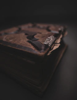 A shadowed close-up of a mysterious leather-bound book glowing softly with a crimson aura.