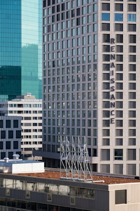High-rise buildings with modern architectural design dominate the skyline. The word 'Renaissance' is prominently displayed on one of the buildings. The structures feature a mix of glass and concrete, reflecting light and casting shadows. Several floors are visible, with a distinctive grid-like pattern of windows.