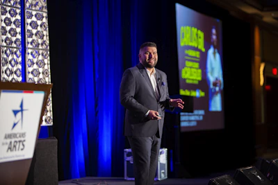 man in black suit standing on stage