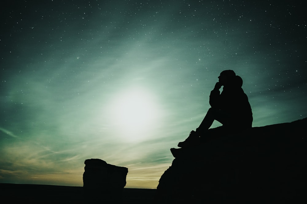 silhouette of woman sitting on rock during night time