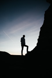 silhouette of man standing on rock during sunset