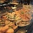 A display of various freshly prepared sandwiches and baked goods, including baguettes filled with lettuce and vegetables, bread rolls, and pretzel sandwiches. The food items are neatly arranged in a glass counter and labeled with small signs indicating their names and prices. There is a selection of flatbreads and pastries placed alongside garnished with fresh herbs.