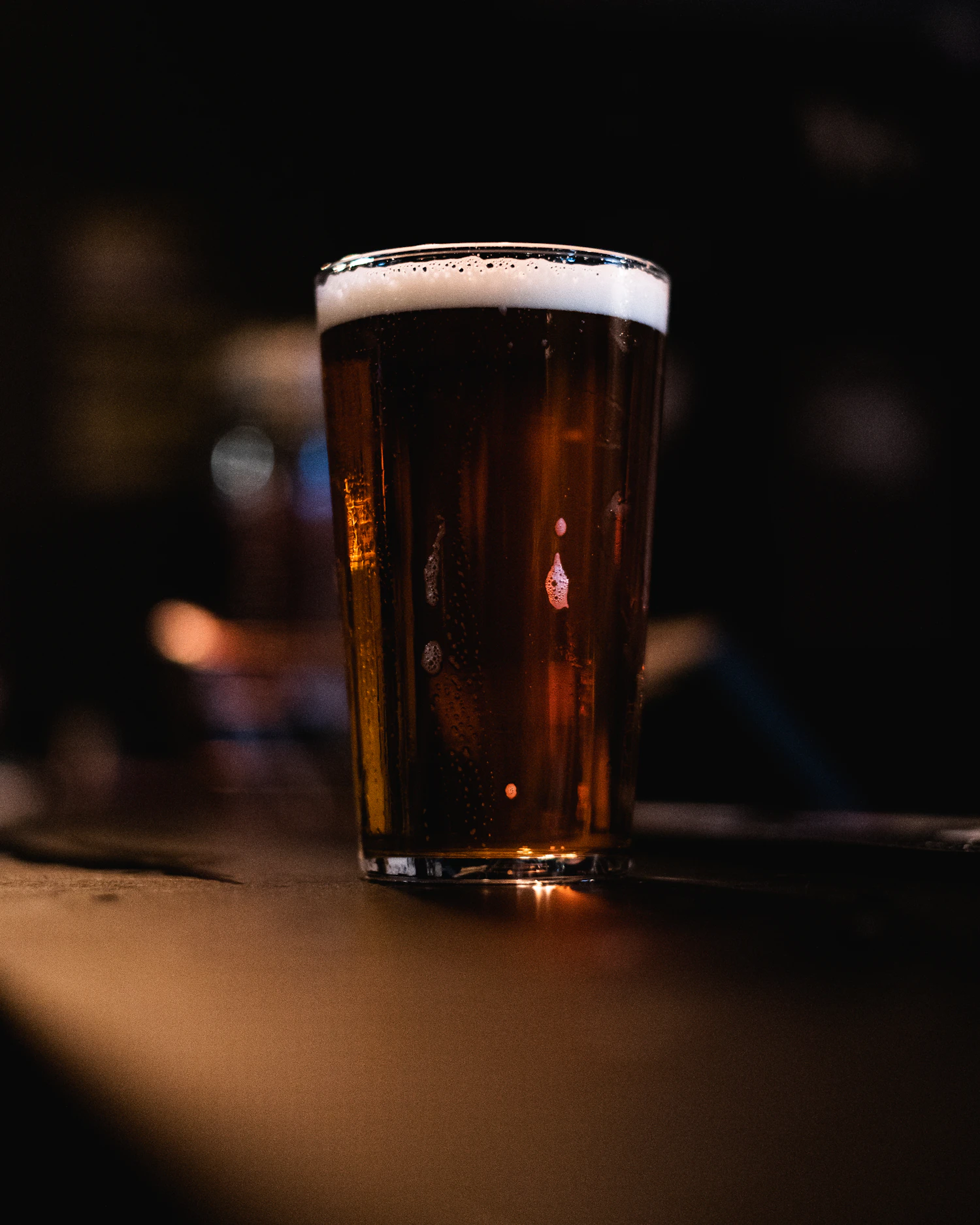 A dark brown porter with a tan head in a pint glass, lit from the side in a dark room