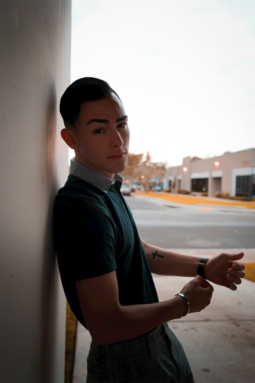 man in black polo shirt standing beside white wall during daytime