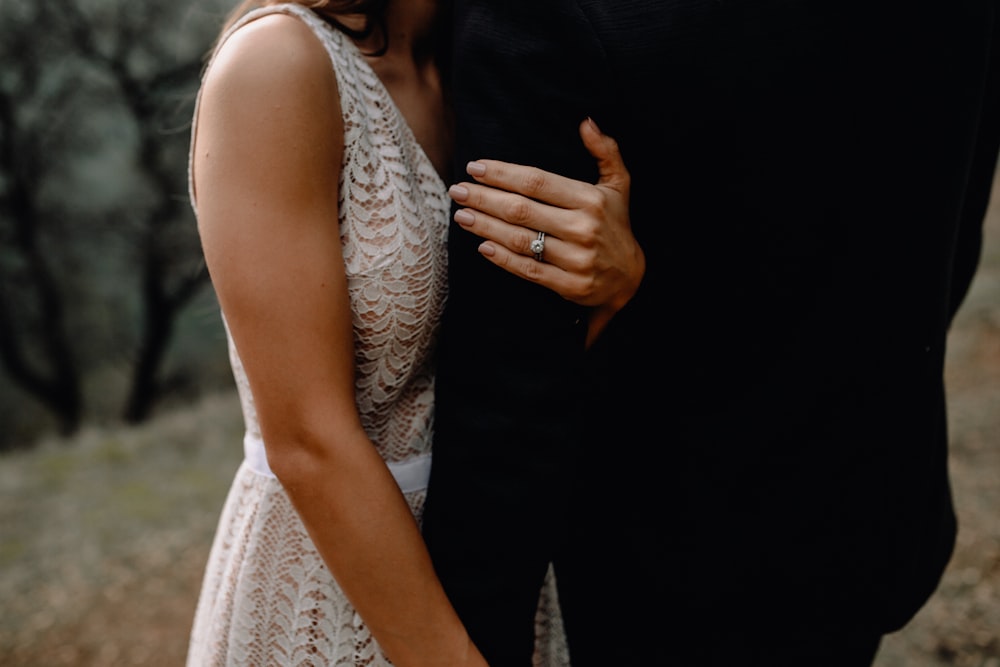woman in white lace sleeveless dress holding man in black suit