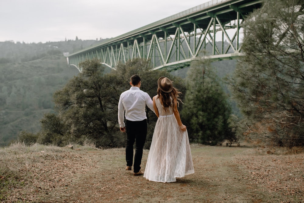 uomo e donna in piedi sul campo di erba marrone vicino al ponte durante il giorno