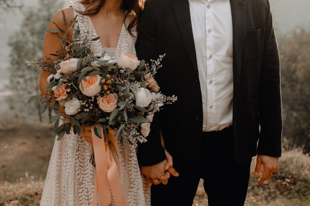 man in black suit holding white flower bouquet