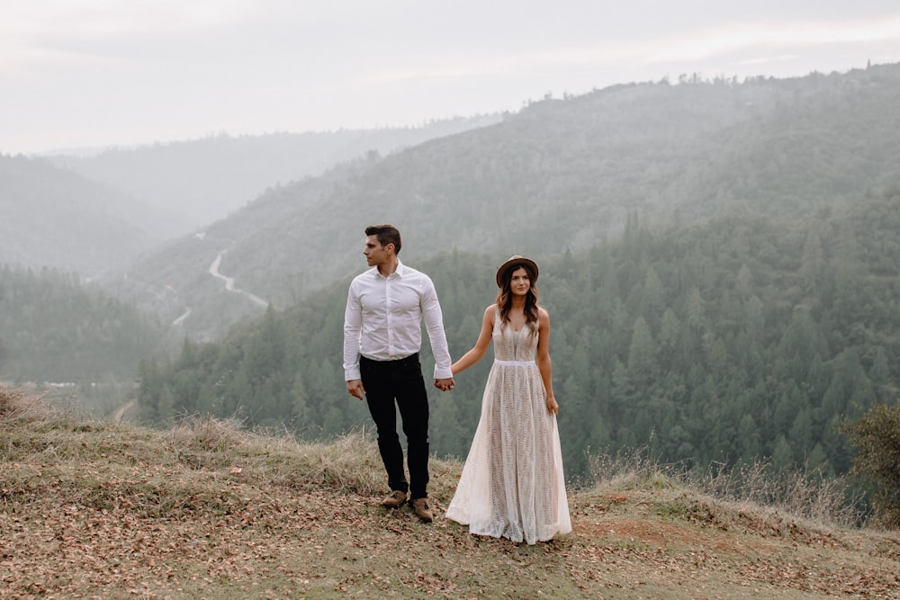 man and woman holding hands while walking on brown grass field during daytime