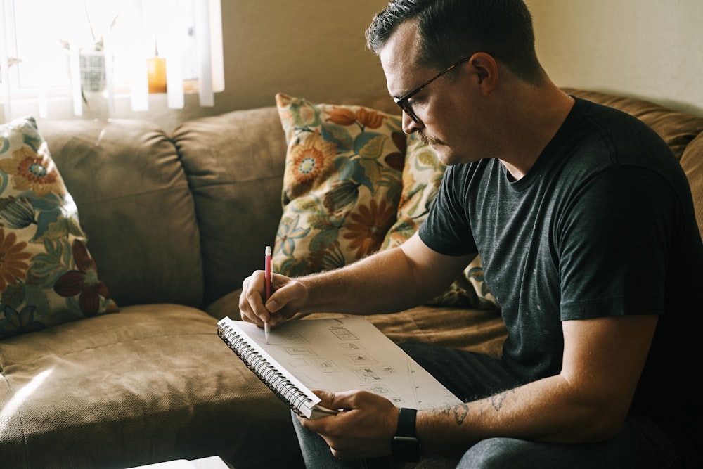 man in black crew neck t-shirt writing on white paper