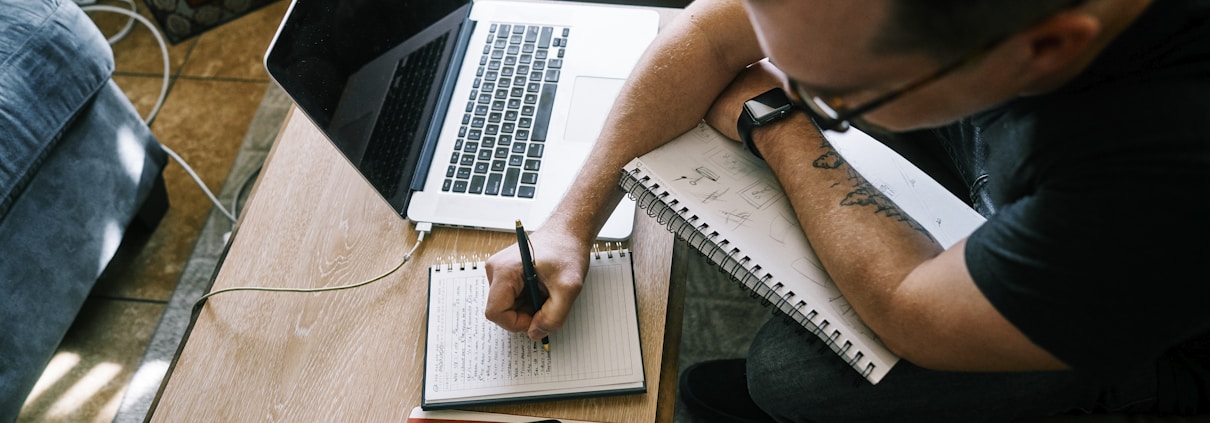 man in black t-shirt writing on white paper