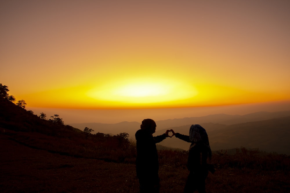 Silhouette von 2 Personen, die bei Sonnenuntergang auf dem Hügel stehen
