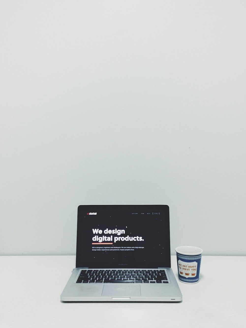 macbook pro beside white and blue plastic cup