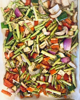 A tray filled with a colorful assortment of chopped vegetables including asparagus, red bell peppers, purple onions, and zucchini, all seasoned with herbs and spices.