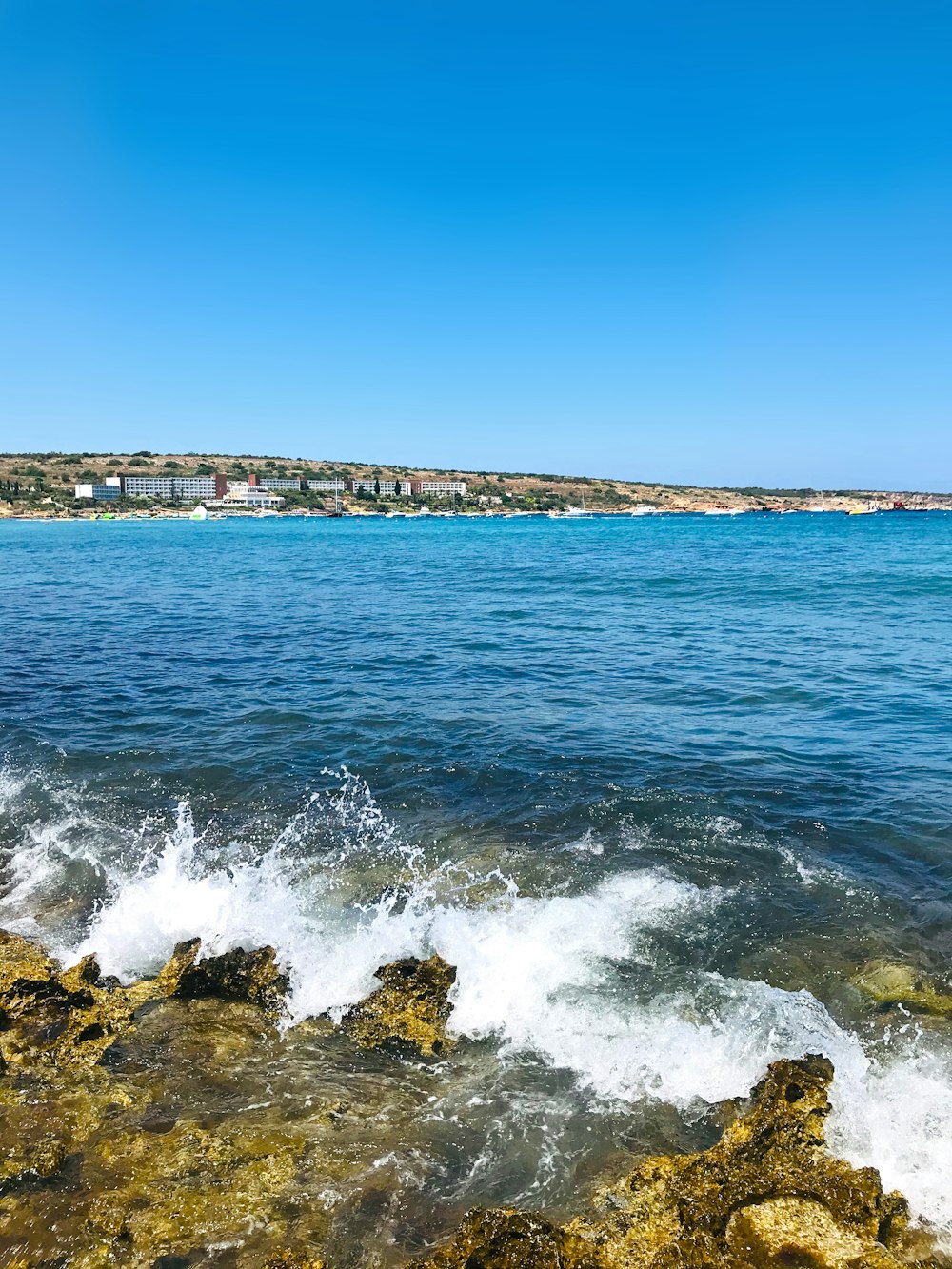 sea waves crashing on rocks under blue sky during daytime