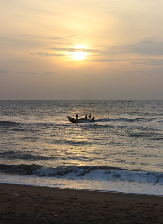 man in white shirt riding white and blue surfboard on sea during sunset in Chennai India