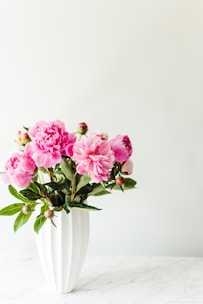 Elegant bouquet of soft pink roses and white peonies arranged in a minimalist vase on a cream background