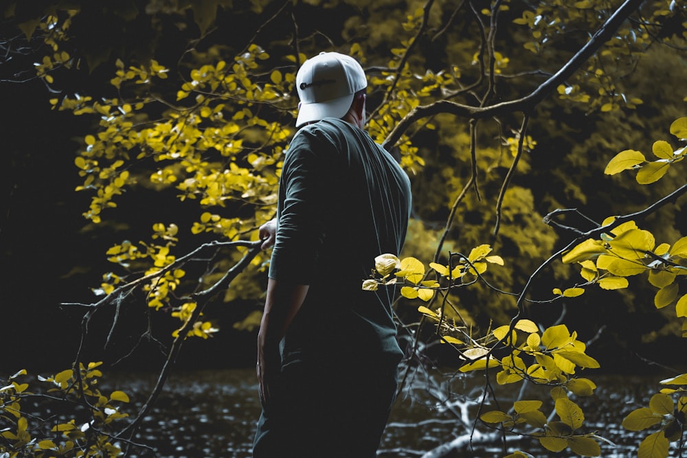 man in black shirt and white cap standing beside yellow leaves during daytime