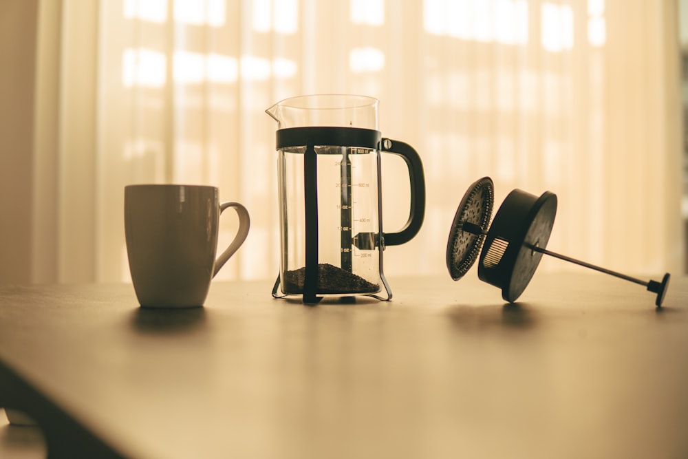 white ceramic mug beside black and silver coffee maker