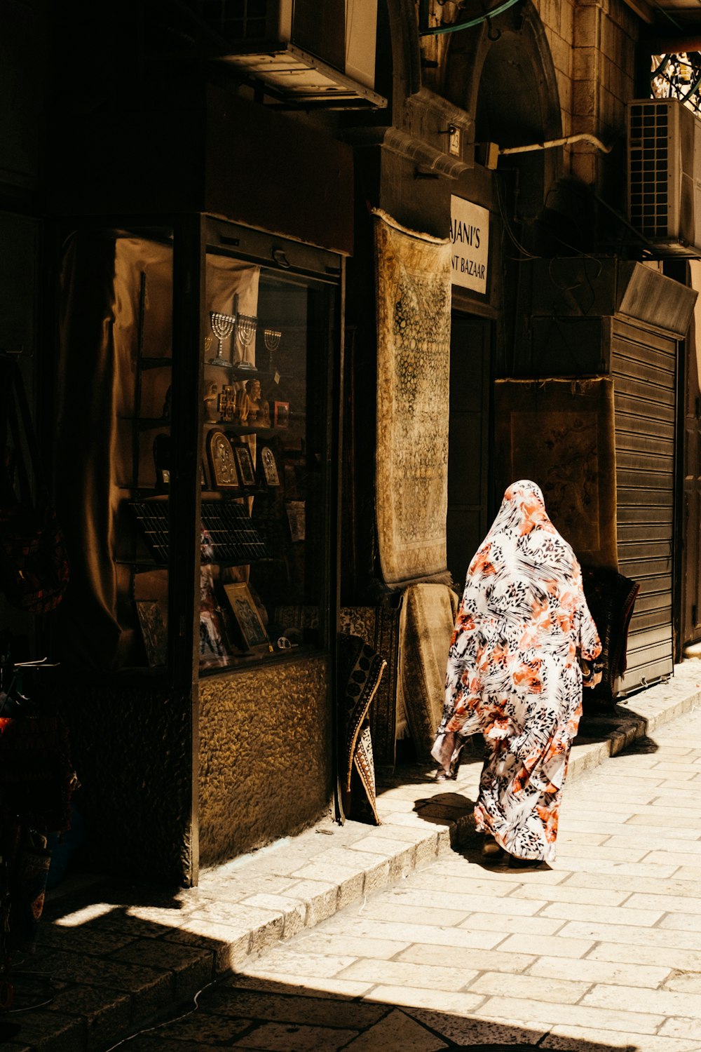 Mujer con hiyab floral blanco y rojo de pie cerca de la tienda