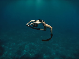 A person is underwater in a graceful pose, wearing flippers and a swimsuit, surrounded by deep blue water.