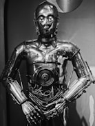 A shiny metallic humanoid robot with intricate details, including visible wires in the midsection. The robot stands in a neutral pose with its arms slightly bent at the elbows.
