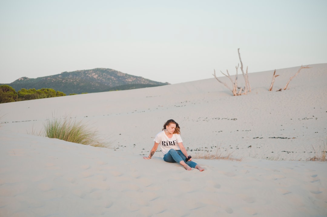 girl in white shirt sitting on white sand during daytime