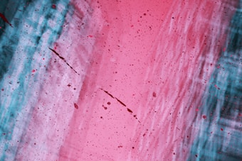 Abstract artwork featuring a mix of vibrant colors with a diagonal division between areas dominated by pink hues and areas dominated by teal hues. Paint splatters are scattered across the canvas, adding dynamic movement.