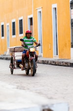 A friendly mototaxi driver helping a passenger with a helmet in a vibrant city street.